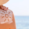 Persona con cappello in spiaggia applica la crema solare sulla spalla con un simbolo del sole – prevenzione contro le scottature solari.